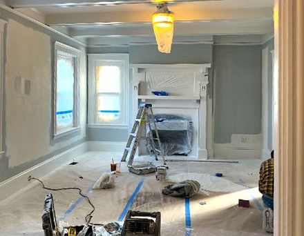 A living room with a fireplace and a ladder in it is being painted.