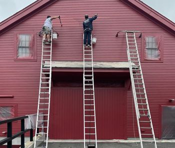 Two men on ladders paint a red building