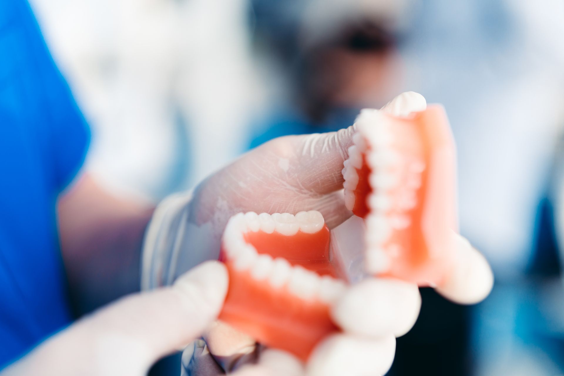 Dentist holding a set of upper and lower dentures with gloved hands.