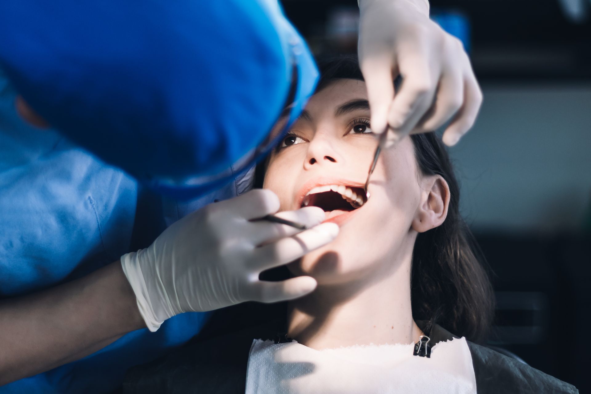 A dentist examines a patient's mouth with tools. Patient is looking up with mouth open.