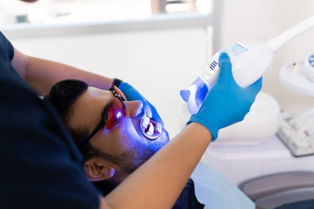 Person in dental chair receiving teeth whitening treatment with blue light.