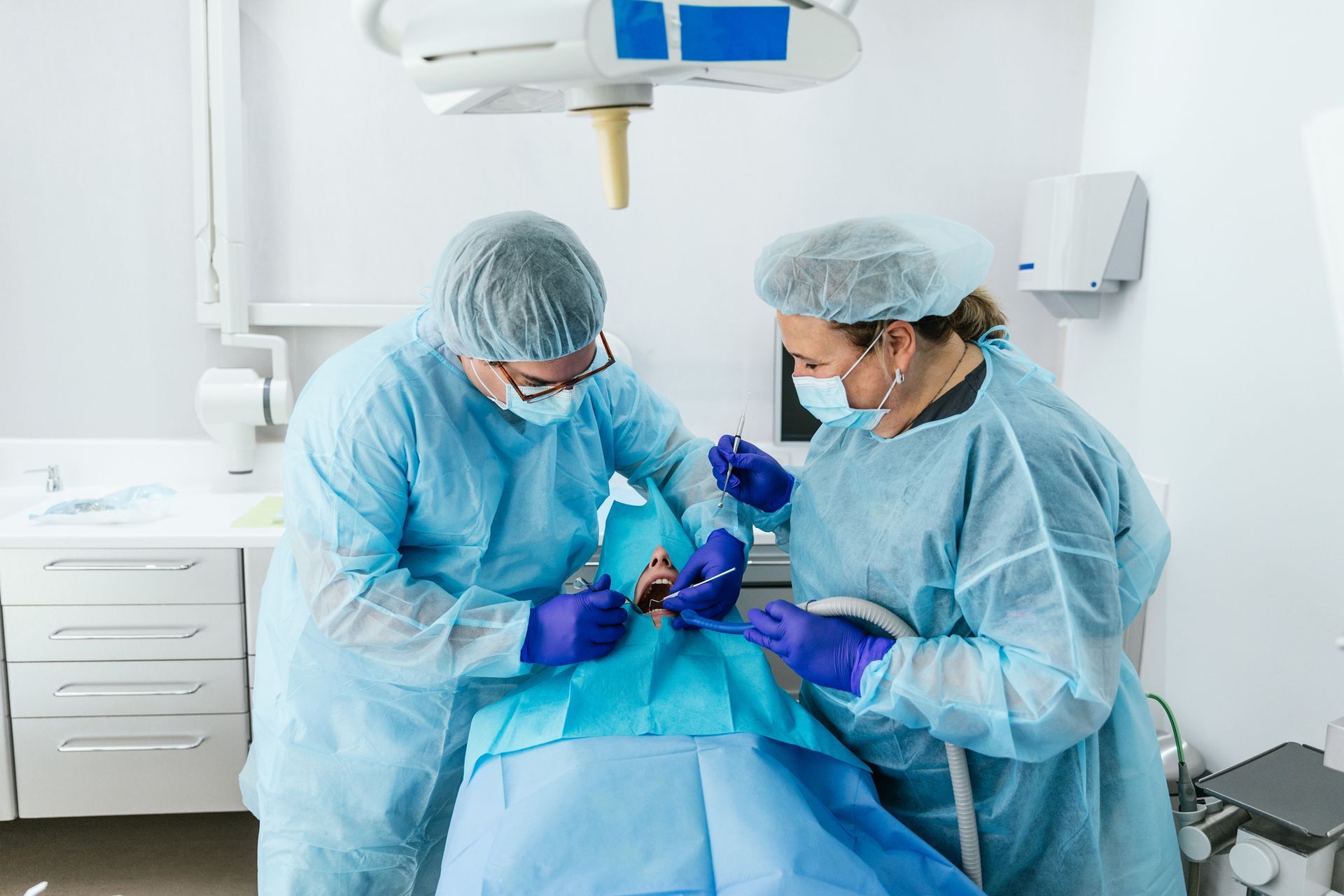 Two surgeons in scrubs perform a dental procedure on a patient in an operating room.