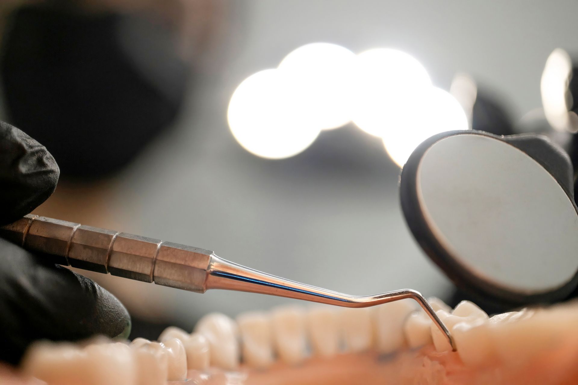 Dentist's gloved hand using a probe and mirror to examine teeth on a model.