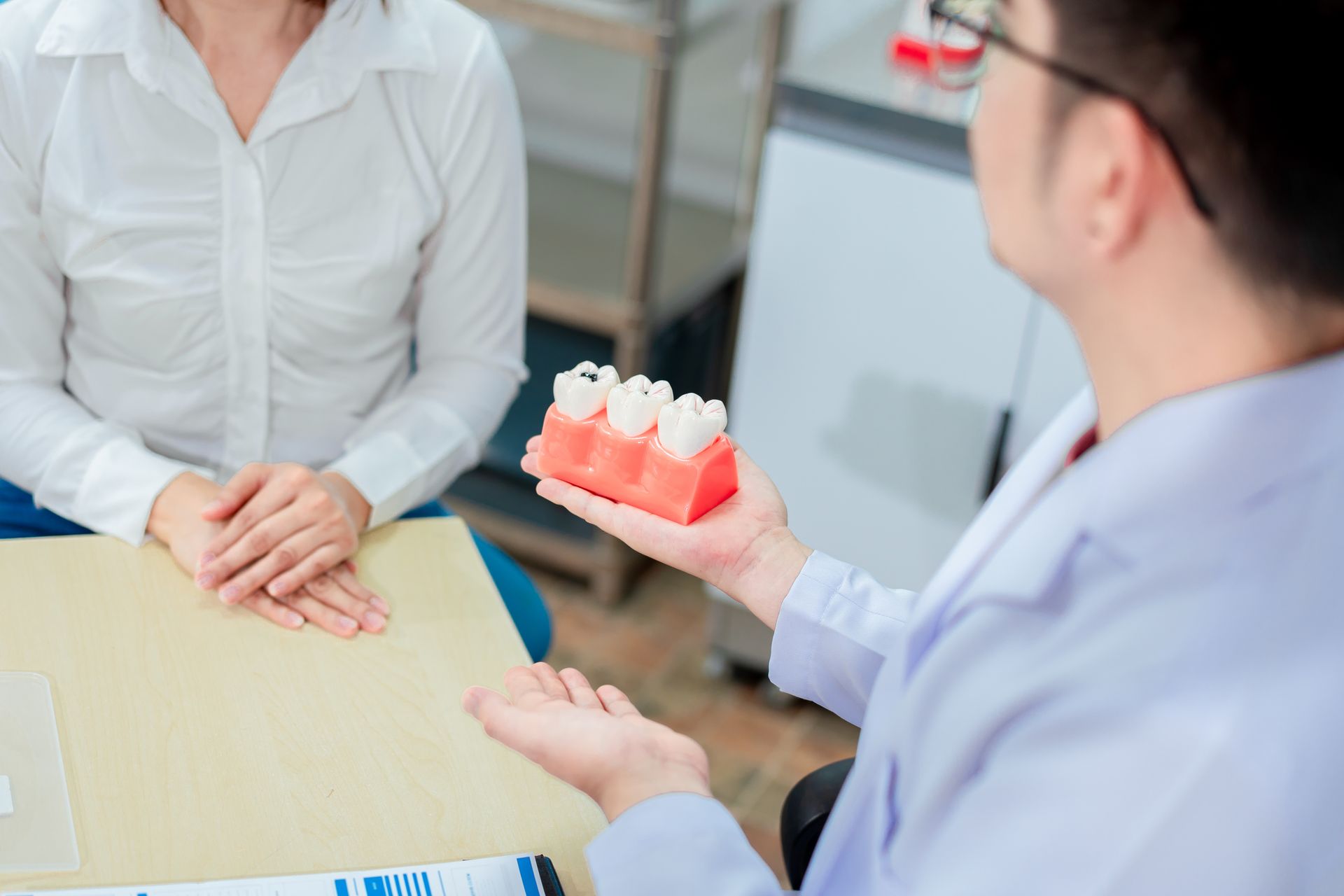 A dentist explains a dental model to a patient in a white-walled office setting.