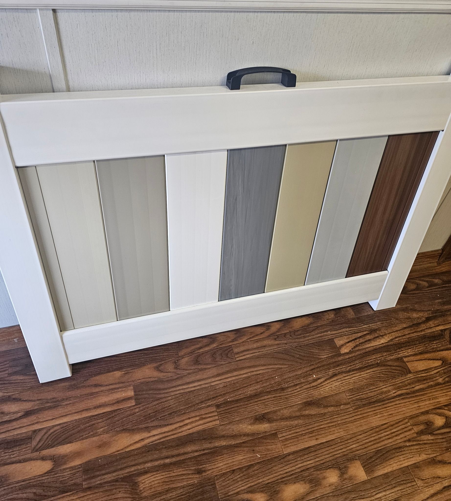 A sample display showing seven vertical flooring or wall panel swatches in various wood and solid neutral finishes.