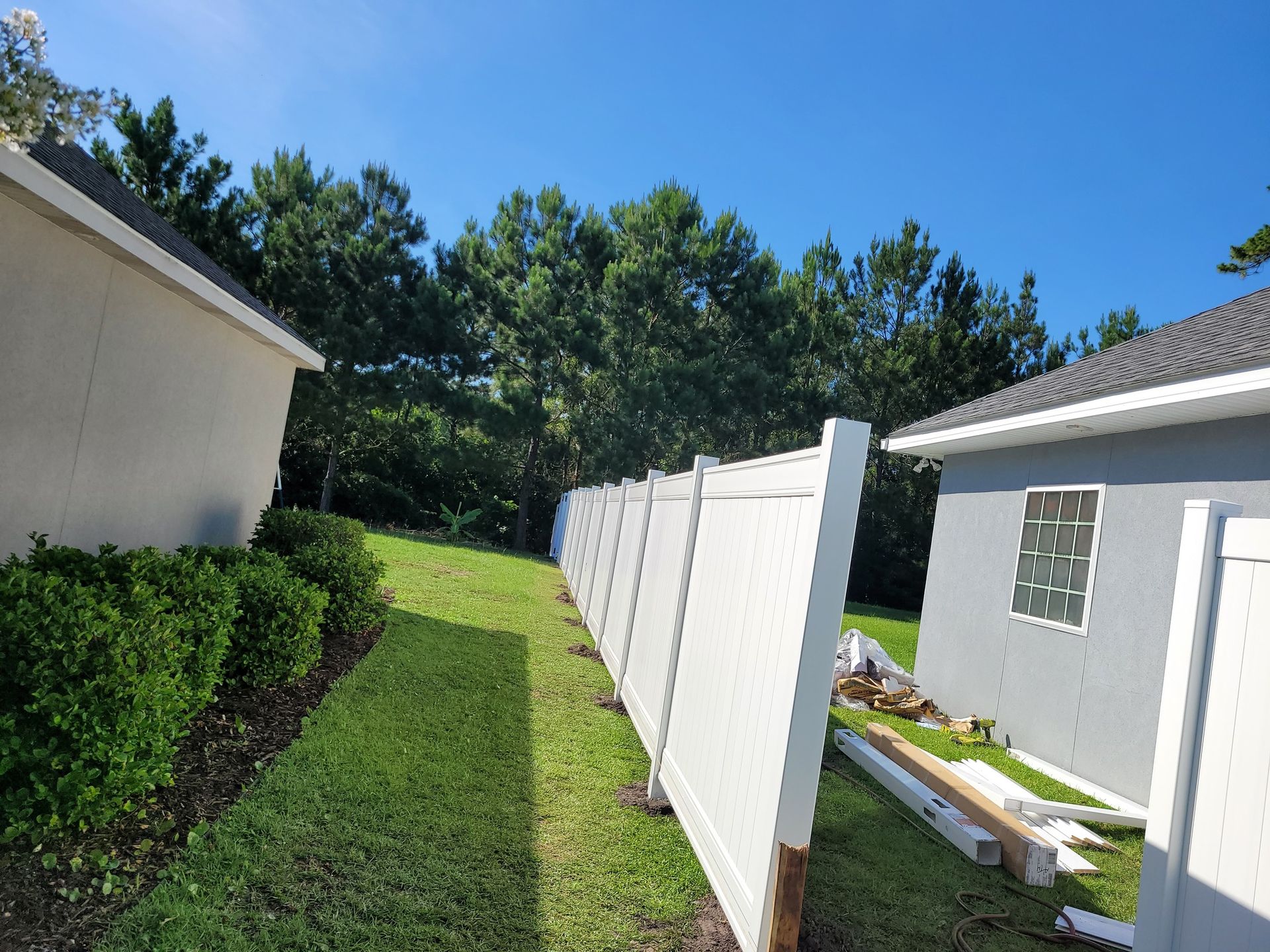 A white vinyl fence runs through a green grassy yard between a beige house and a gray house with a decorative tile piece.