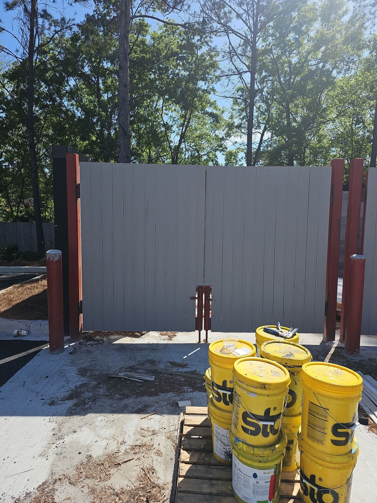 A grey wooden gate stands outdoors with several yellow Sto-branded construction buckets stacked on a wooden pallet.
