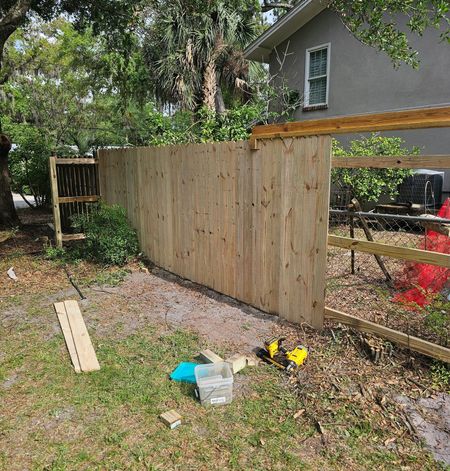 A wooden privacy fence under construction in a grassy yard near a house, with a few scattered construction tools.