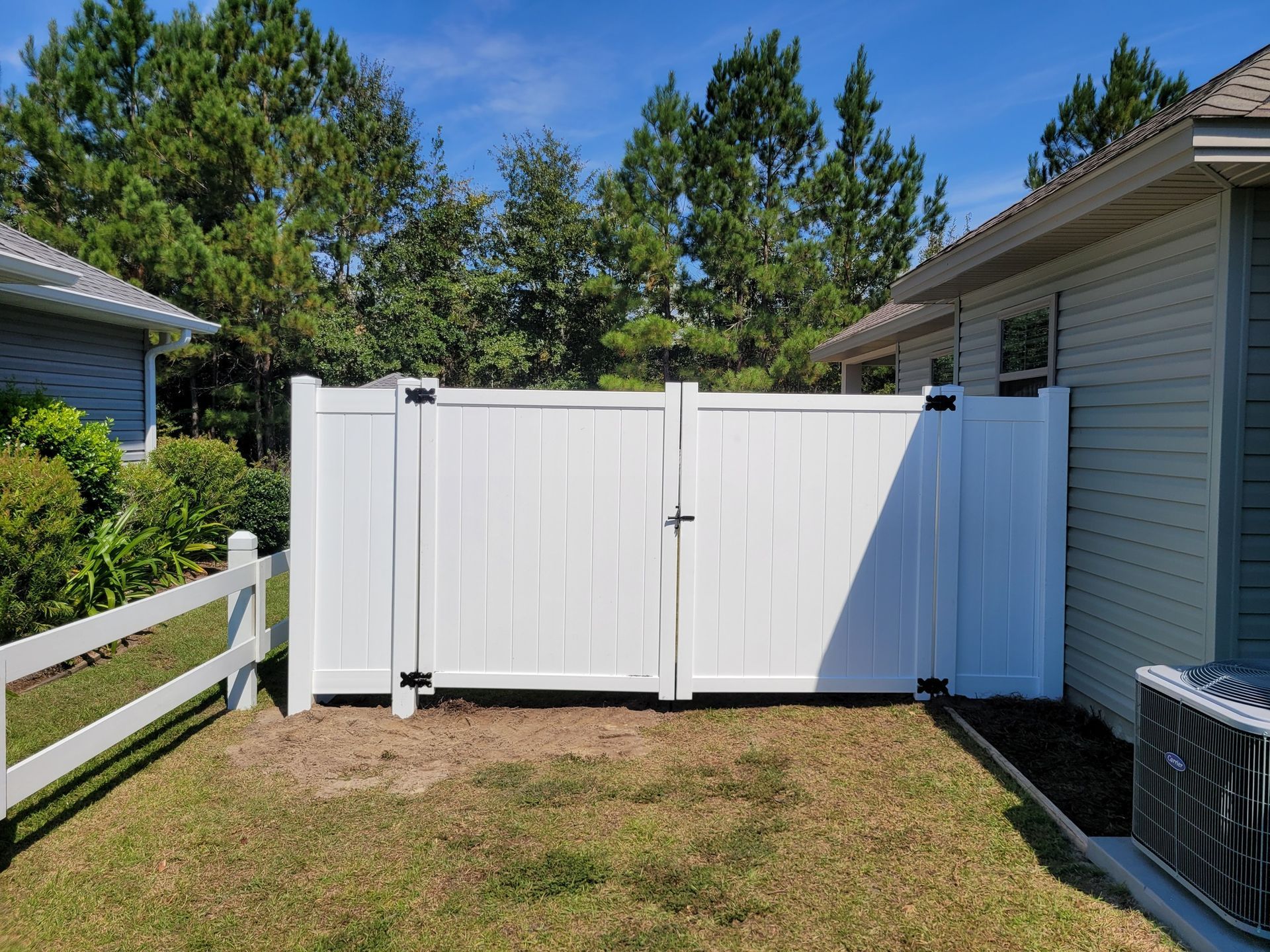 A white vinyl privacy gate is installed between the side of a beige house and an existing yard fence.