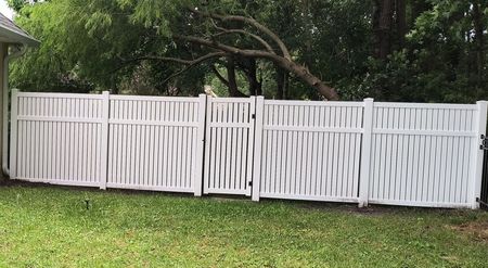 A white privacy fence with a unique woven-style lattice pattern, featuring a gate in the center, set against a lawn.