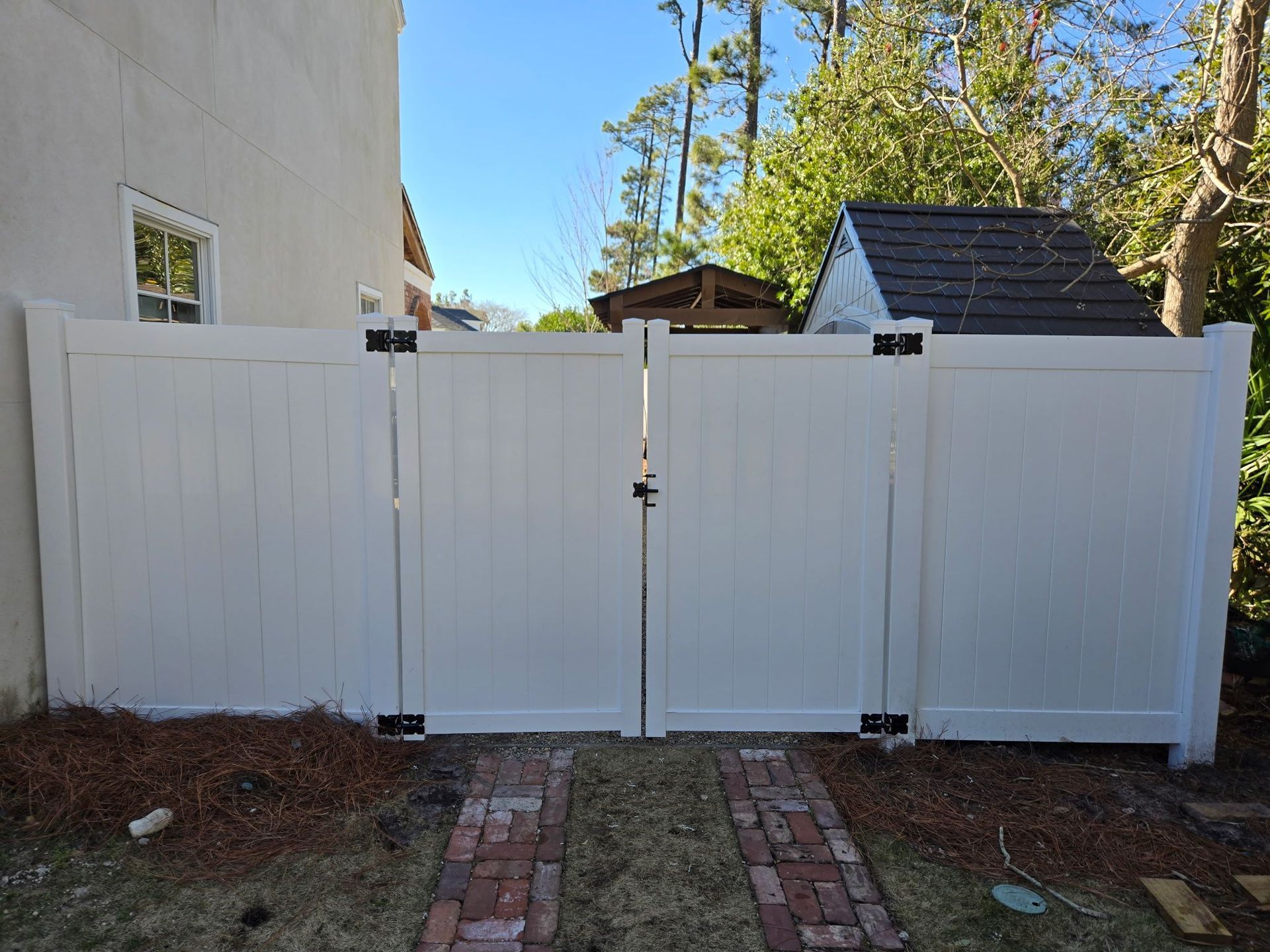A white vinyl fence with a double-gate entrance in a residential yard.