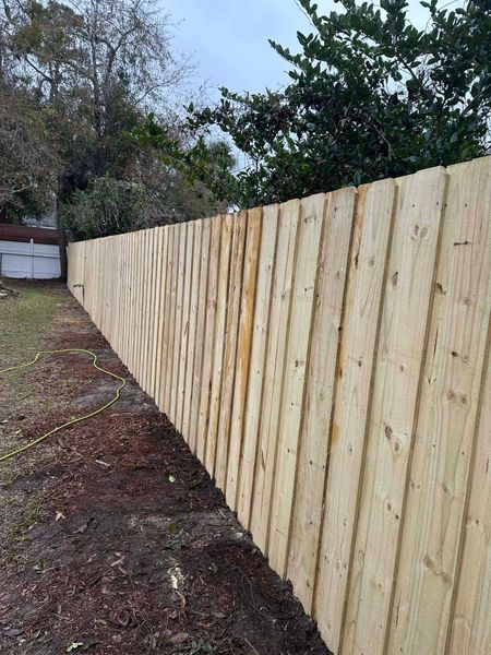 A new wooden privacy fence runs along a yard edge with mulch and trees in the background.