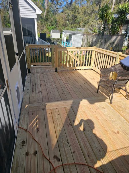 A newly built wooden deck with railings and a small gate, viewed from a doorway, with a chair and a human shadow visible.