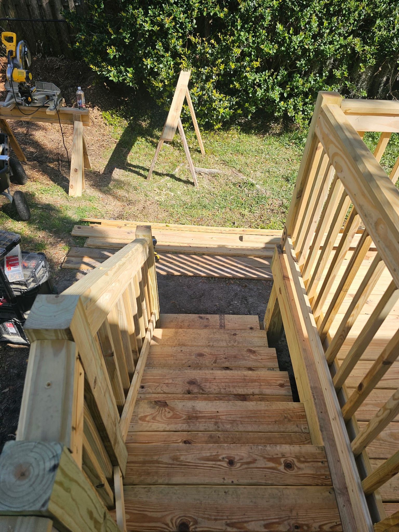Wooden outdoor stairs leading down from a deck to a grassy backyard with construction equipment visible on the left.