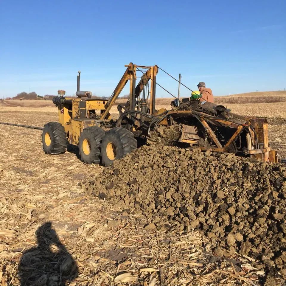 Yellow tractor plowing dry field, turning rough soil under a clear blue sky.