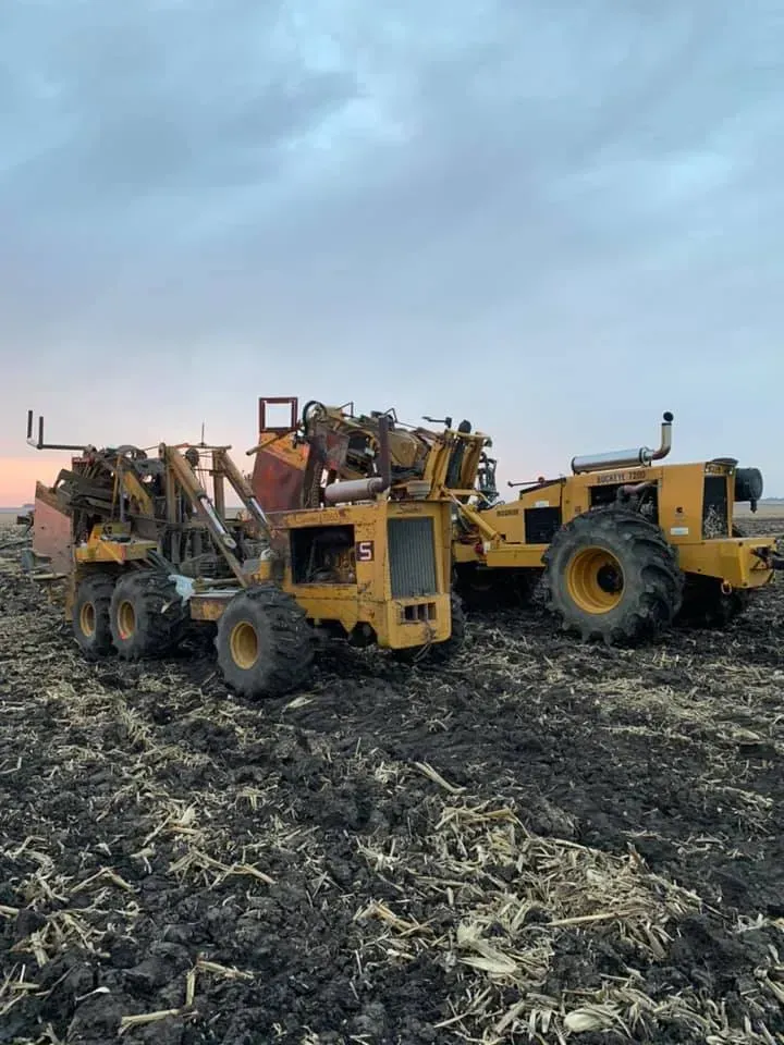 Two yellow industrial vehicles in a muddy field under a cloudy sky