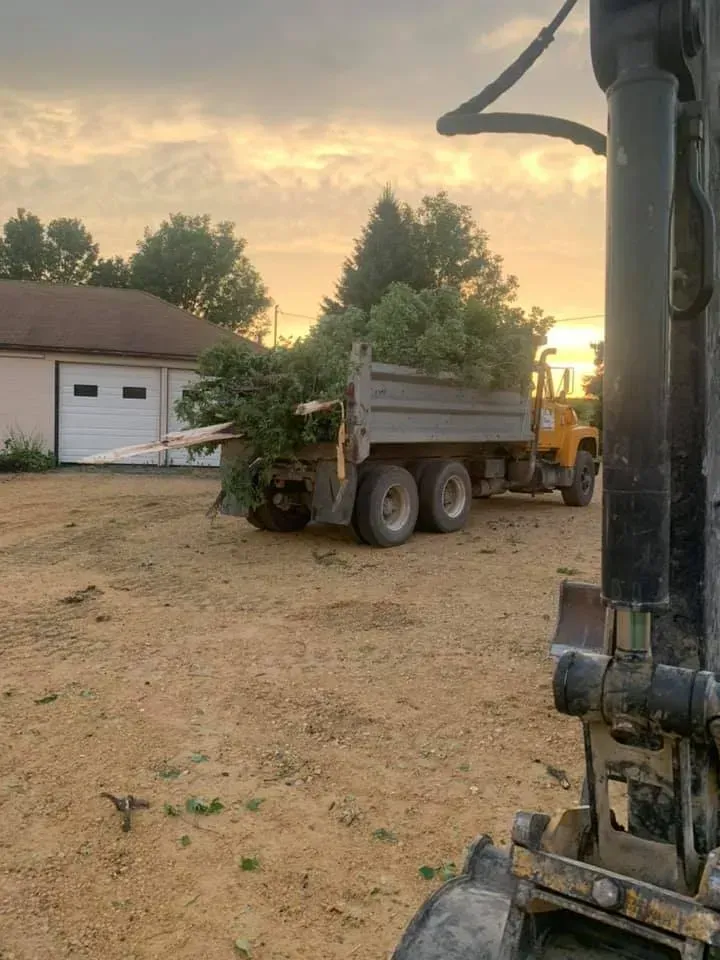 Dump truck parked on a dirt lot at sunset beside a garage and trees