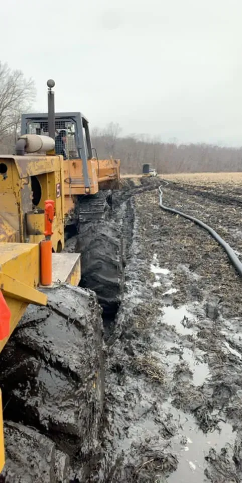 Yellow excavator working beside a muddy railroad track on a snowy, overcast day
