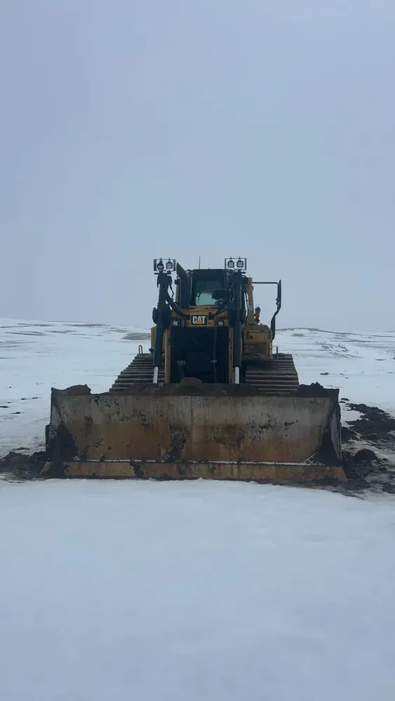 Bulldozer pushing snow on a frozen, snow-covered landscape under a gray sky