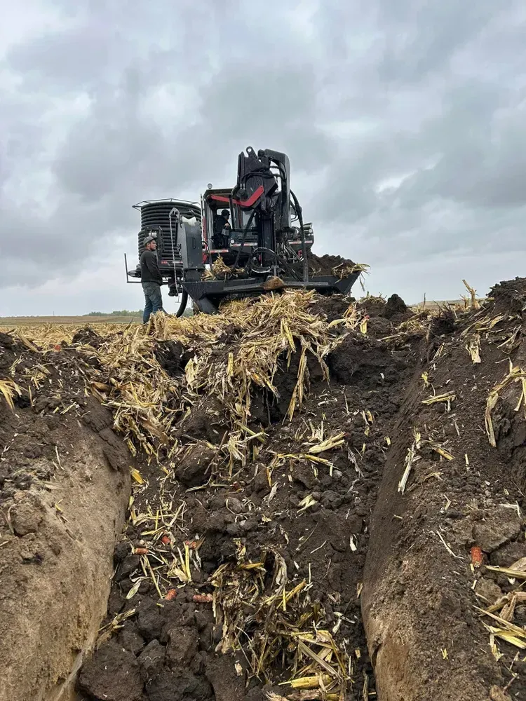 Tracked harvester on muddy farm field under cloudy sky, cutting through crop residue