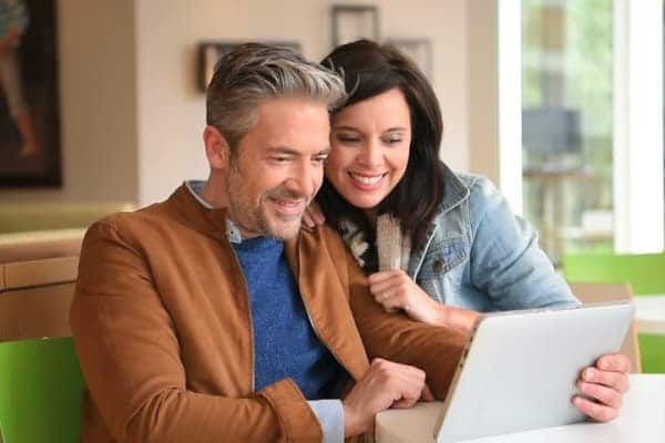 A man and a woman are sitting at a table looking at a laptop.