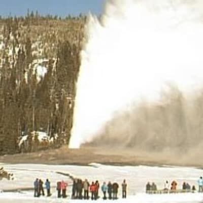 A group of people are standing in front of a large geyser.