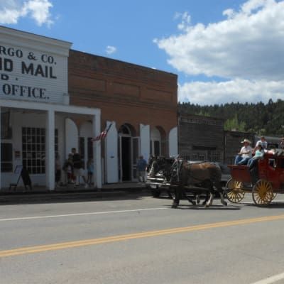 A horse drawn carriage is driving down the street in front of a post office