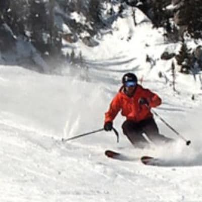 A man in an orange jacket is skiing down a snow covered slope.