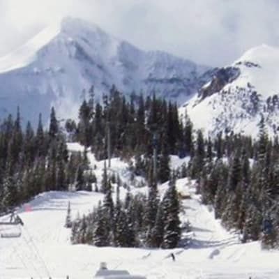 A ski lift is going down a snow covered slope with mountains in the background.