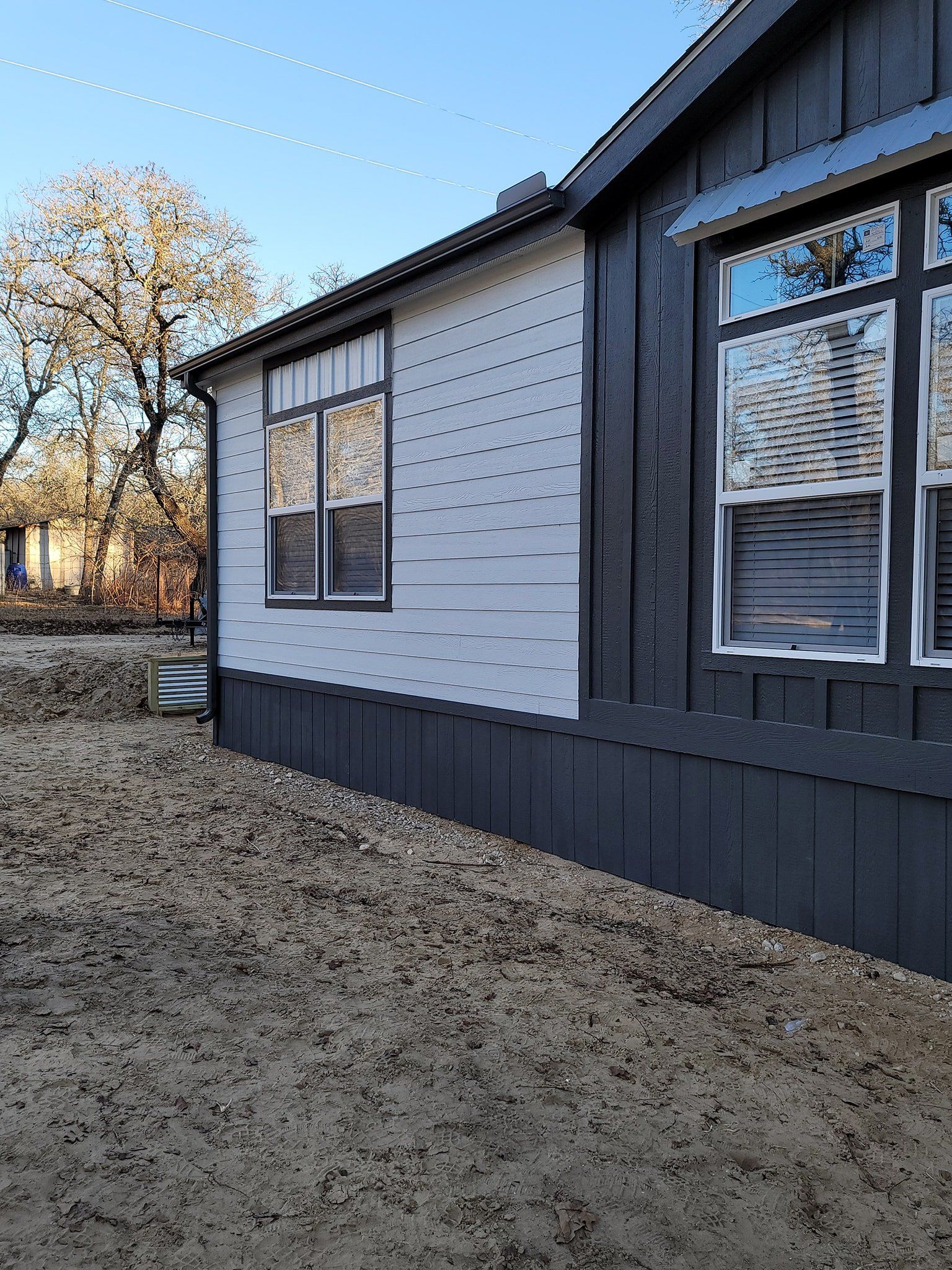 Dark grey and white house exterior with windows, siding, and exposed gravel yard.