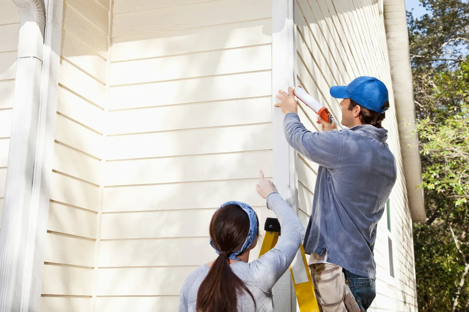 A man and a woman are working on the side of a house.