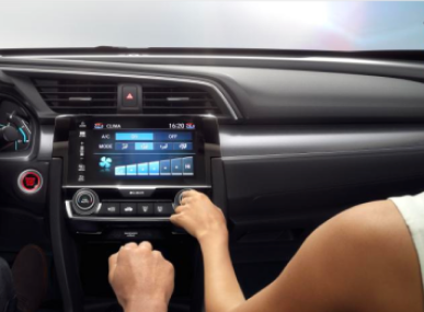 Mãos ajustando o controle climático do painel de um carro.