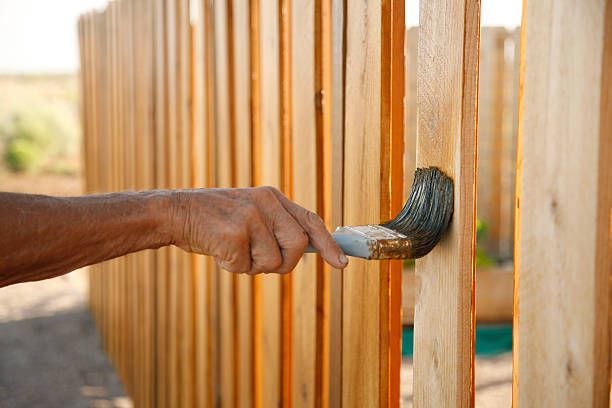 A person is painting a wooden fence with a brush.