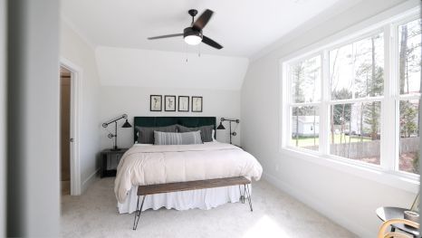 A bedroom with a bed , ceiling fan , and large windows.