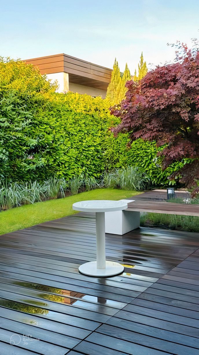 A white table is sitting on a wooden deck in a garden.