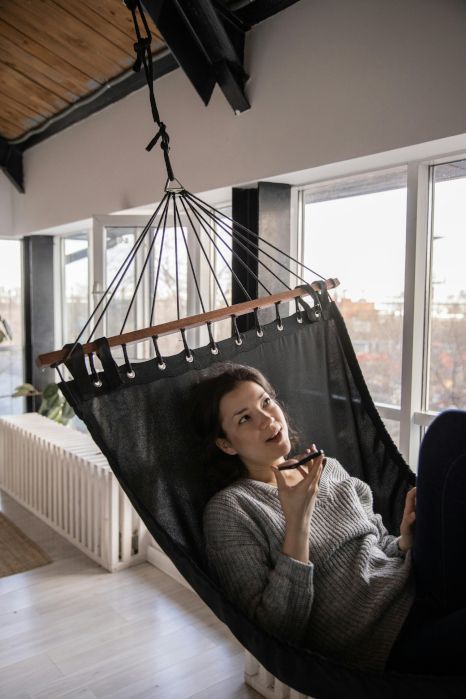 A woman is laying in a hammock in front of a window.