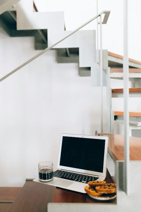 A laptop computer is sitting on a table next to stairs. Expertly painted by Orchid Decor in Newport, Wales.