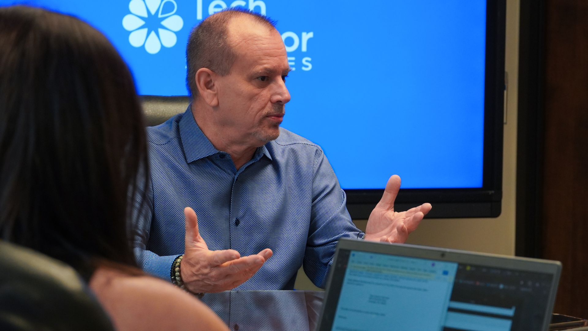 A group of people are sitting around a table with laptops having a meeting.