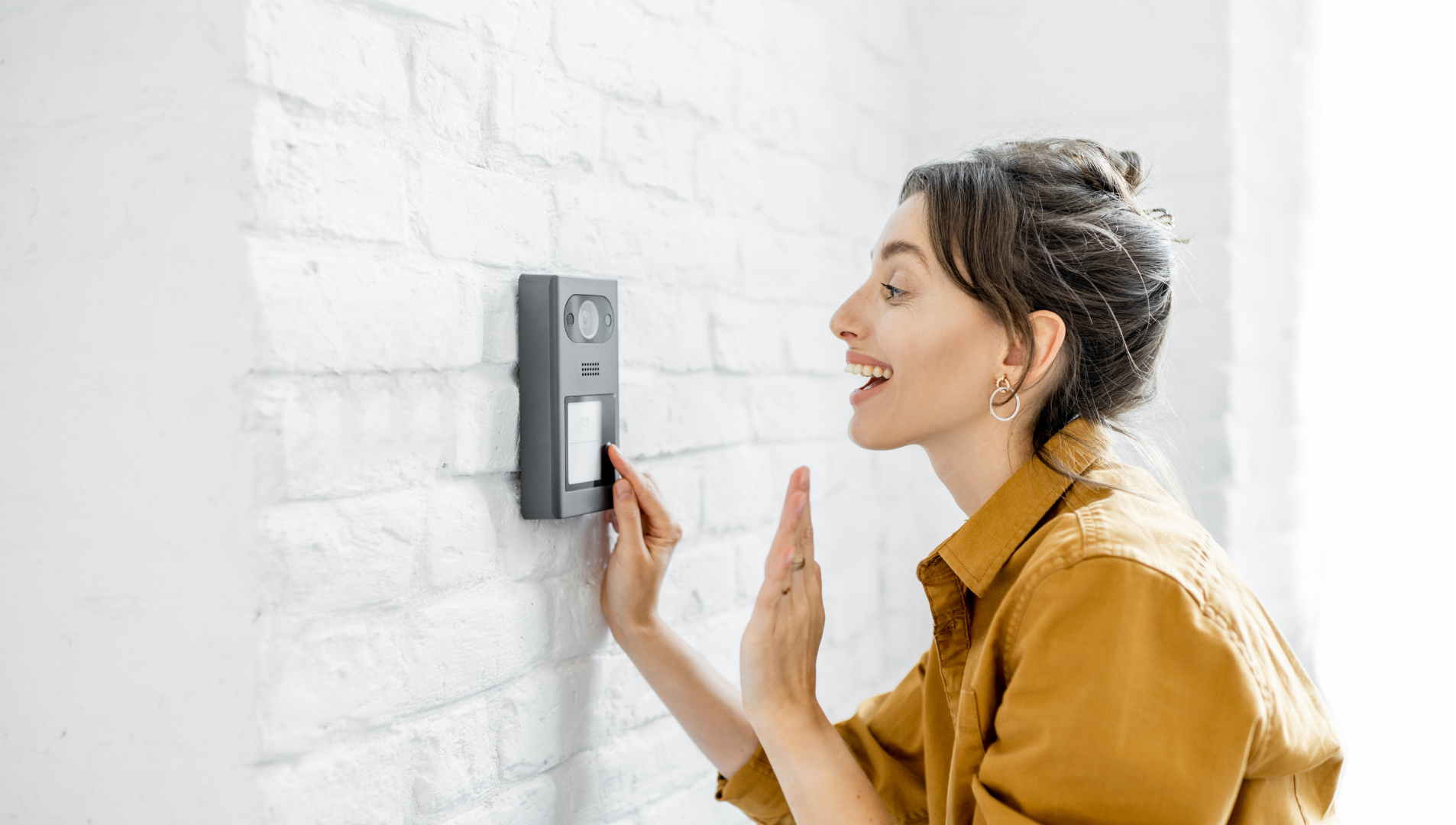 Woman using a wall-mounted intercom against a white brick wall