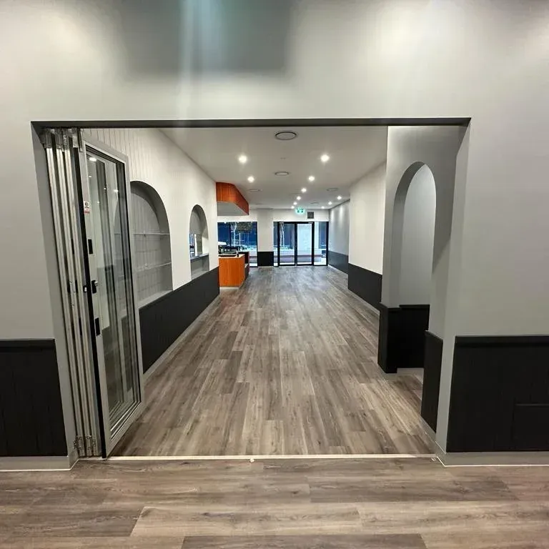 A wide, empty commercial space with light wood floors, grey walls, dark baseboards, and arched decorative wall cutouts.