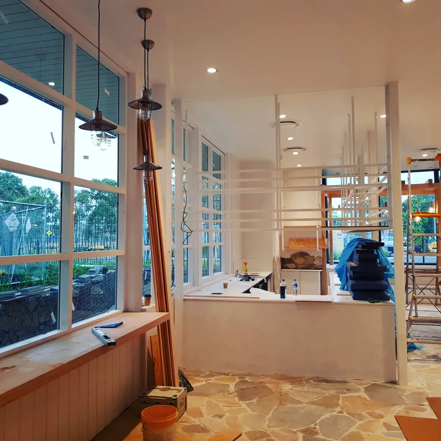 An interior view of a bright, modern commercial space under construction with floor-to-ceiling windows and stone floors.