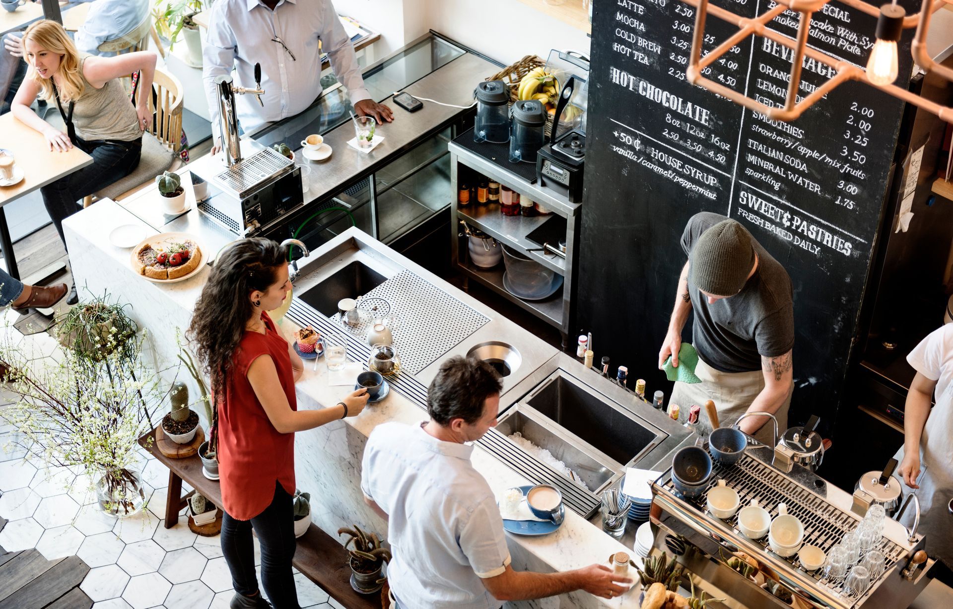 High-angle view of a busy coffee shop with staff preparing drinks and customers waiting at the counter.