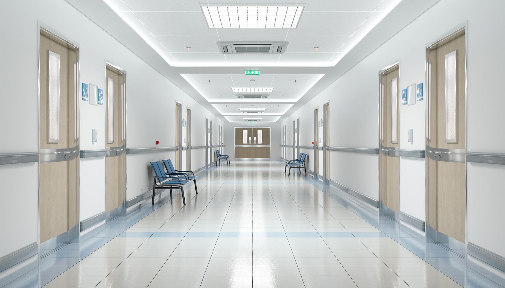 A bright, empty hospital hallway with white walls, tiled floors, wooden doors on both sides, and rows of blue chairs.