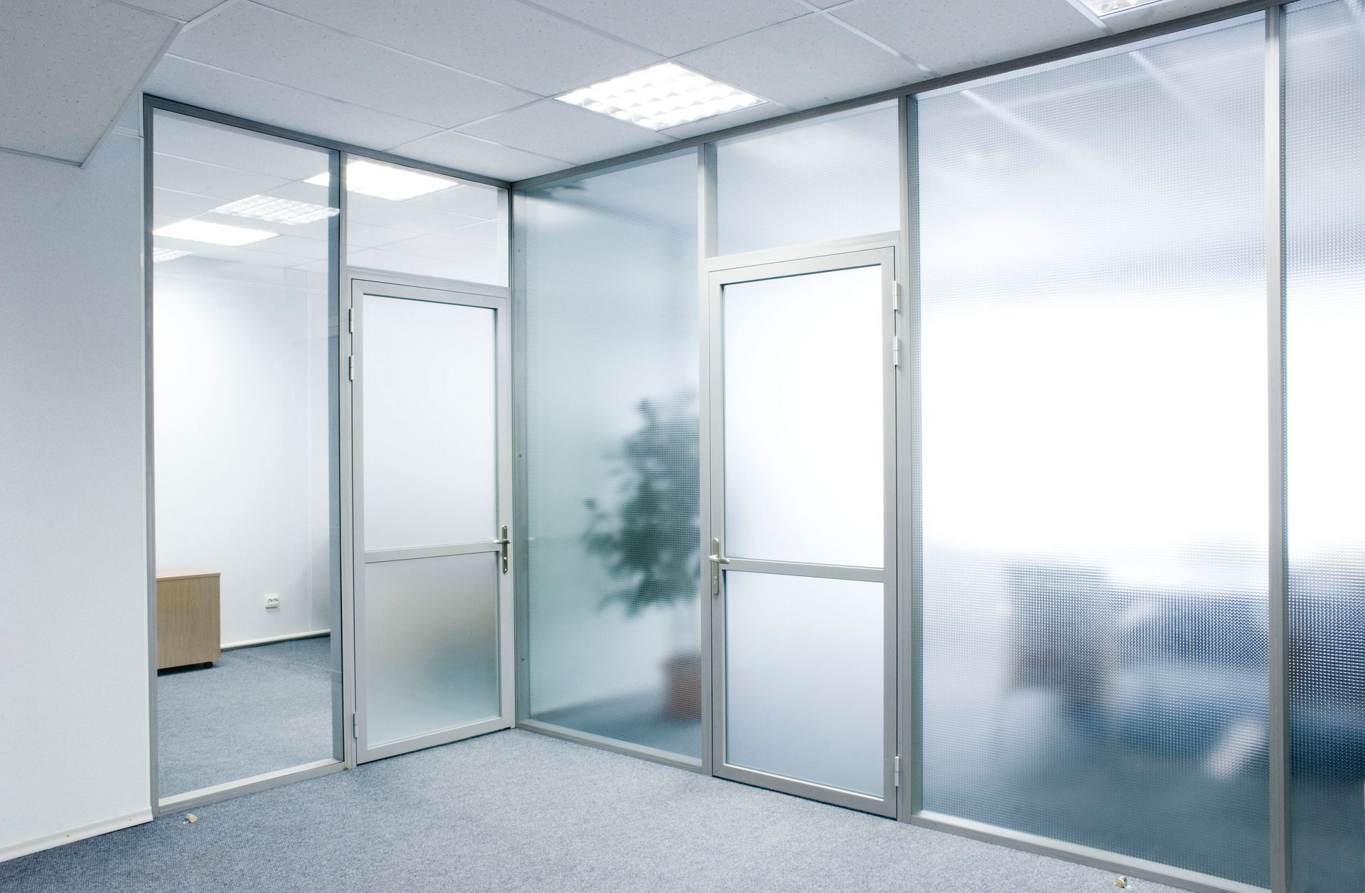 Modern office interior featuring glass partitions and doors, with frosted and ribbed glass panels separating workspace.