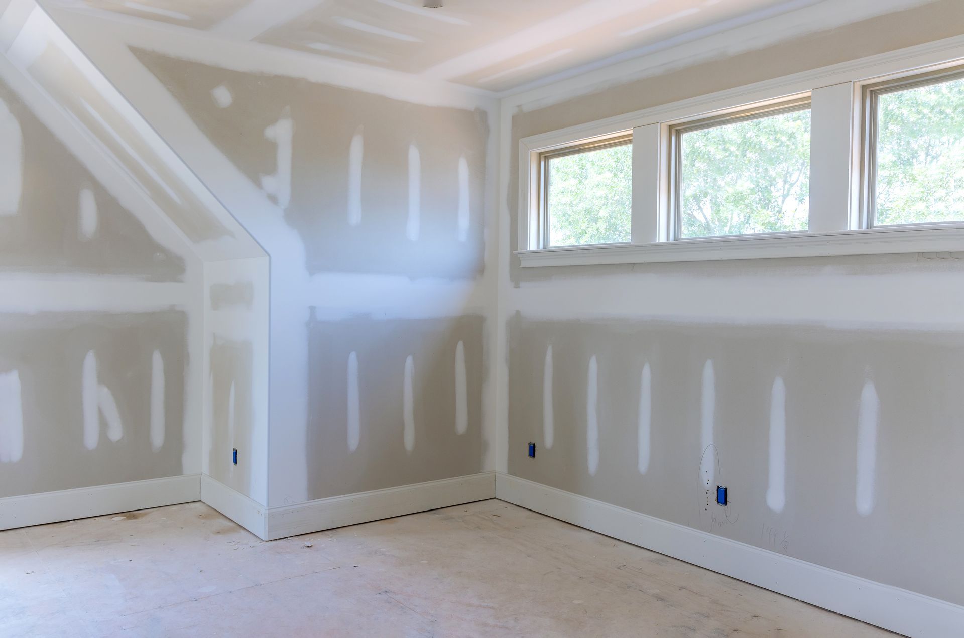 Unfinished room with drywall, taped seams, white trim, and a set of windows along a wall.