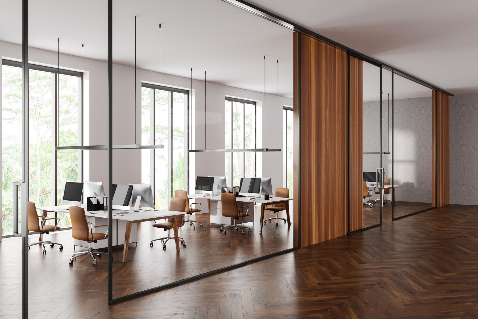 Modern office with desks, computer workstations, and glass partition walls over a herringbone wood floor.