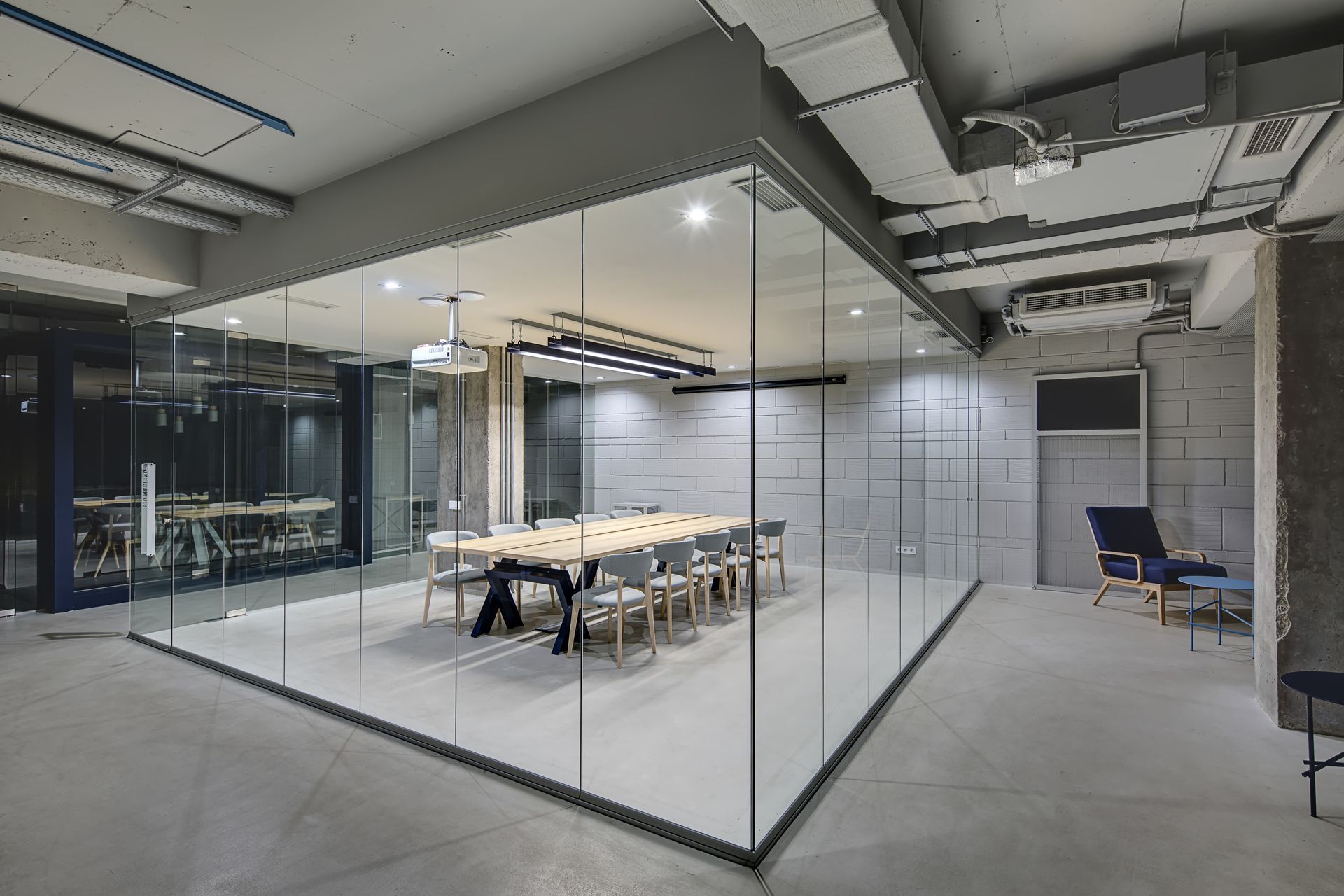 A modern glass-walled conference room with a long table and chairs inside, set within an industrial office space.