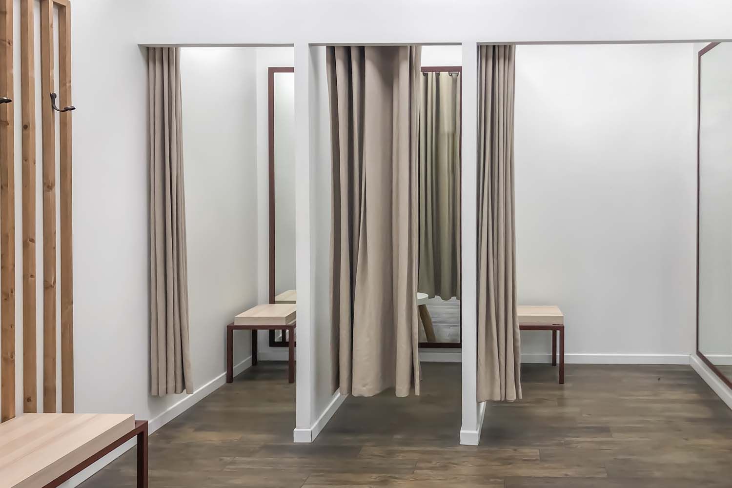 A bright dressing room area with three curtained stalls, light-colored wooden benches, and light wood wall slats.