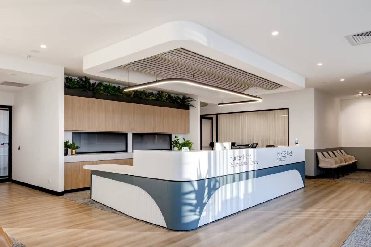 Modern reception desk in a bright office, featuring a curved blue and white counter, wood cabinets, and overhead lighting.
