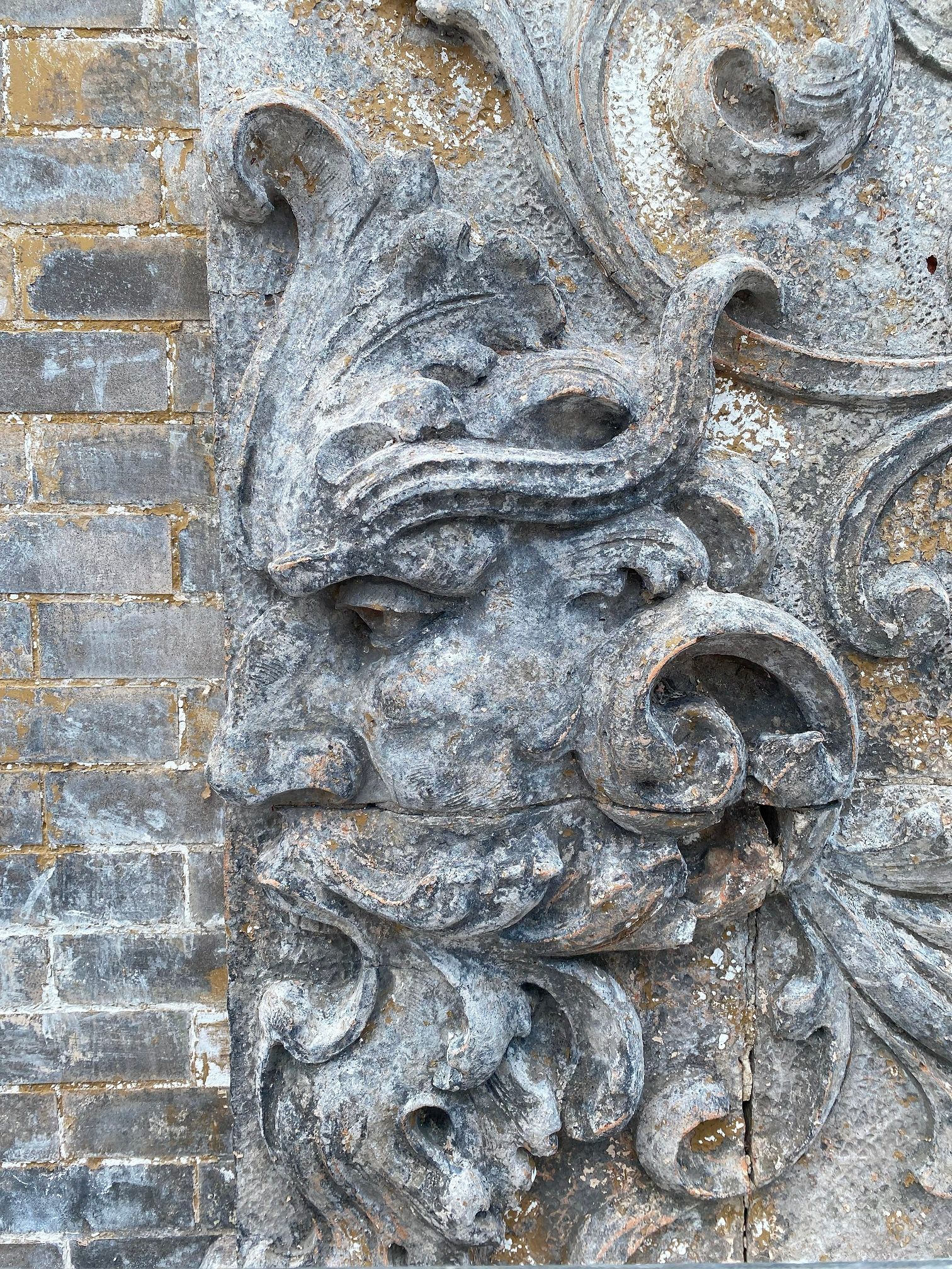 Gray stone carving of a floral face motif on a brick wall
